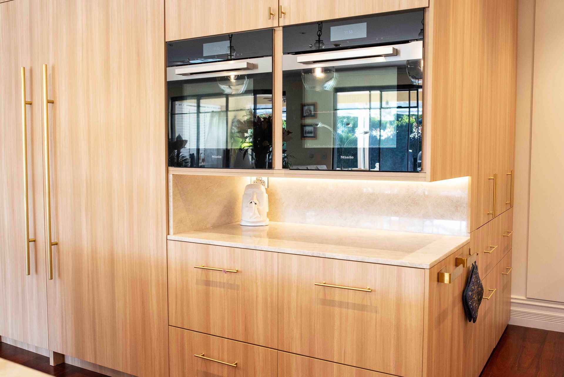 Kitchen cabinetry with wood grain finish, integrated double ovens, and gold hardware.