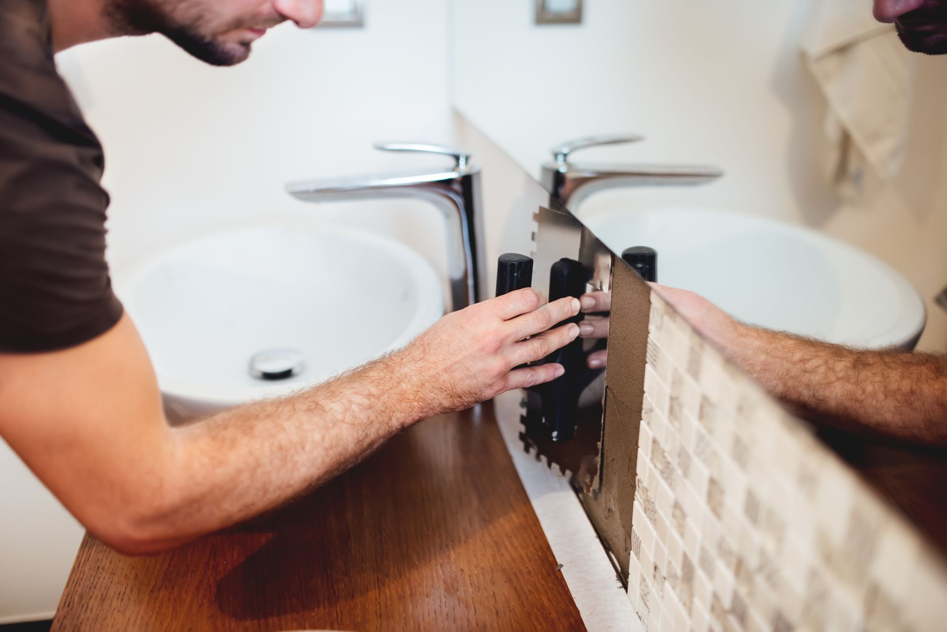 A builder installing mosaic tiles and using an industrial trowel in a modern bathroom.