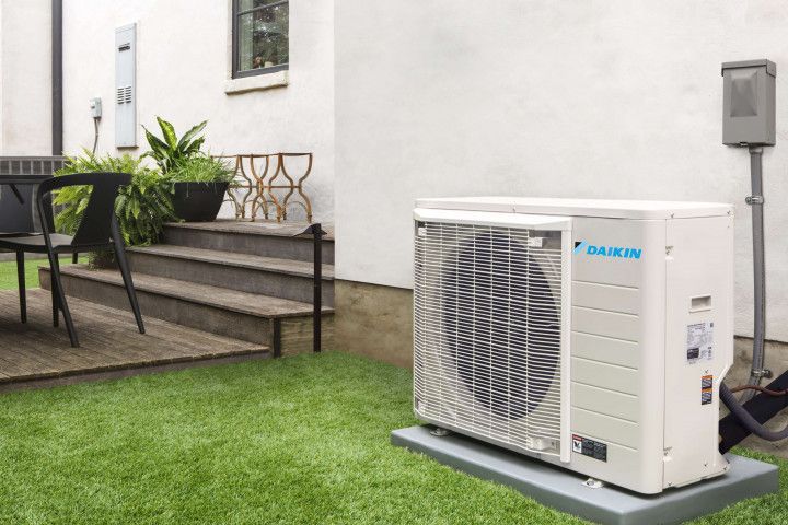 A daikin air conditioner is sitting on the grass in front of a house.