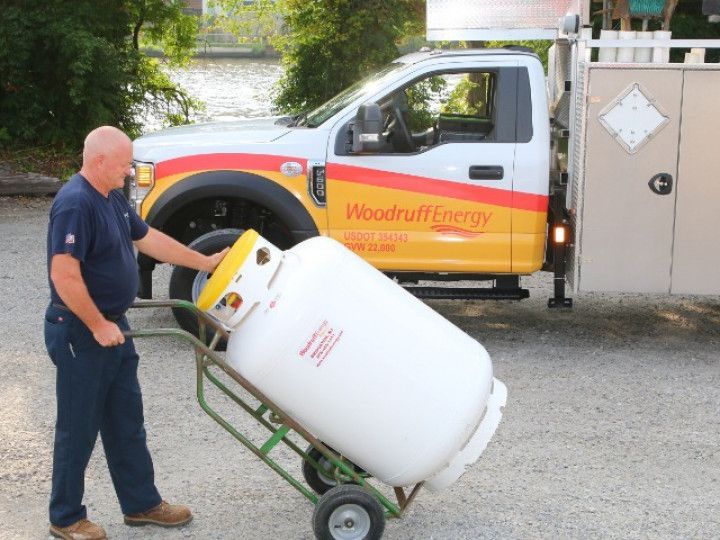 A man pushing a propane tank on a cart in front of a woodruff energy truck