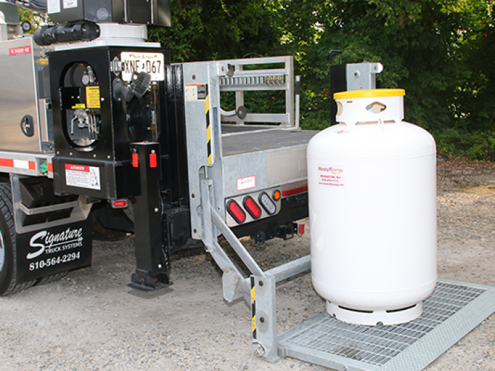 A propane tank is sitting on a metal platform next to a truck