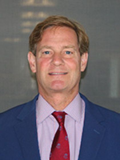 A man in a blue suit and red tie is smiling for the camera.