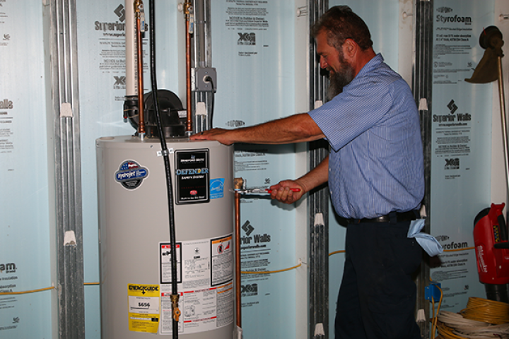 A man is working on a water heater in a basement.