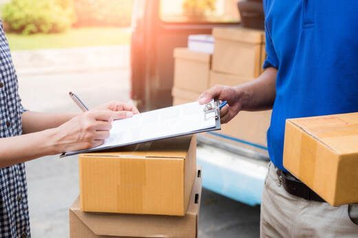 Person signing for a delivery of cardboard boxes from a delivery person in front of a van.