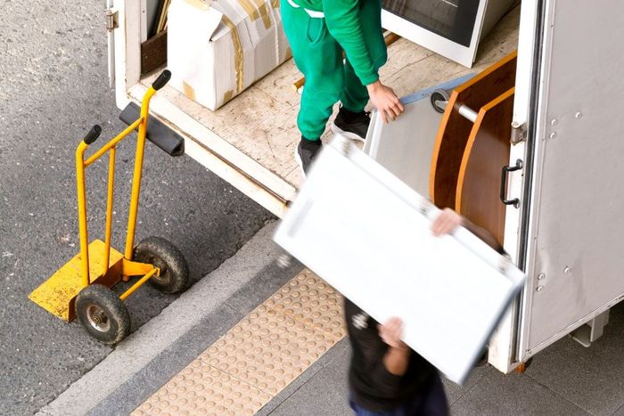 Movers loading furniture into a truck; one person carries a white panel, another stands inside.