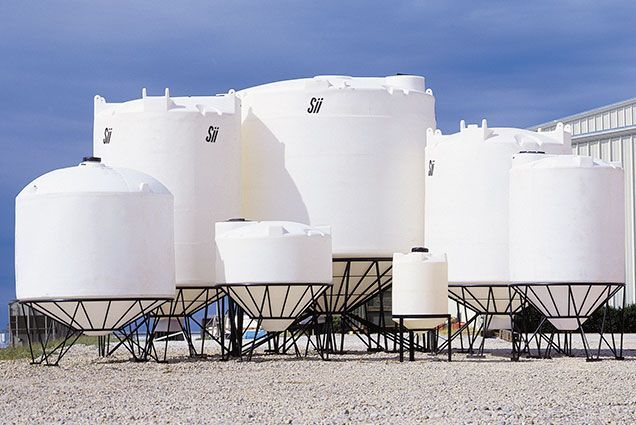 A group of white tanks are lined up in a gravel area.