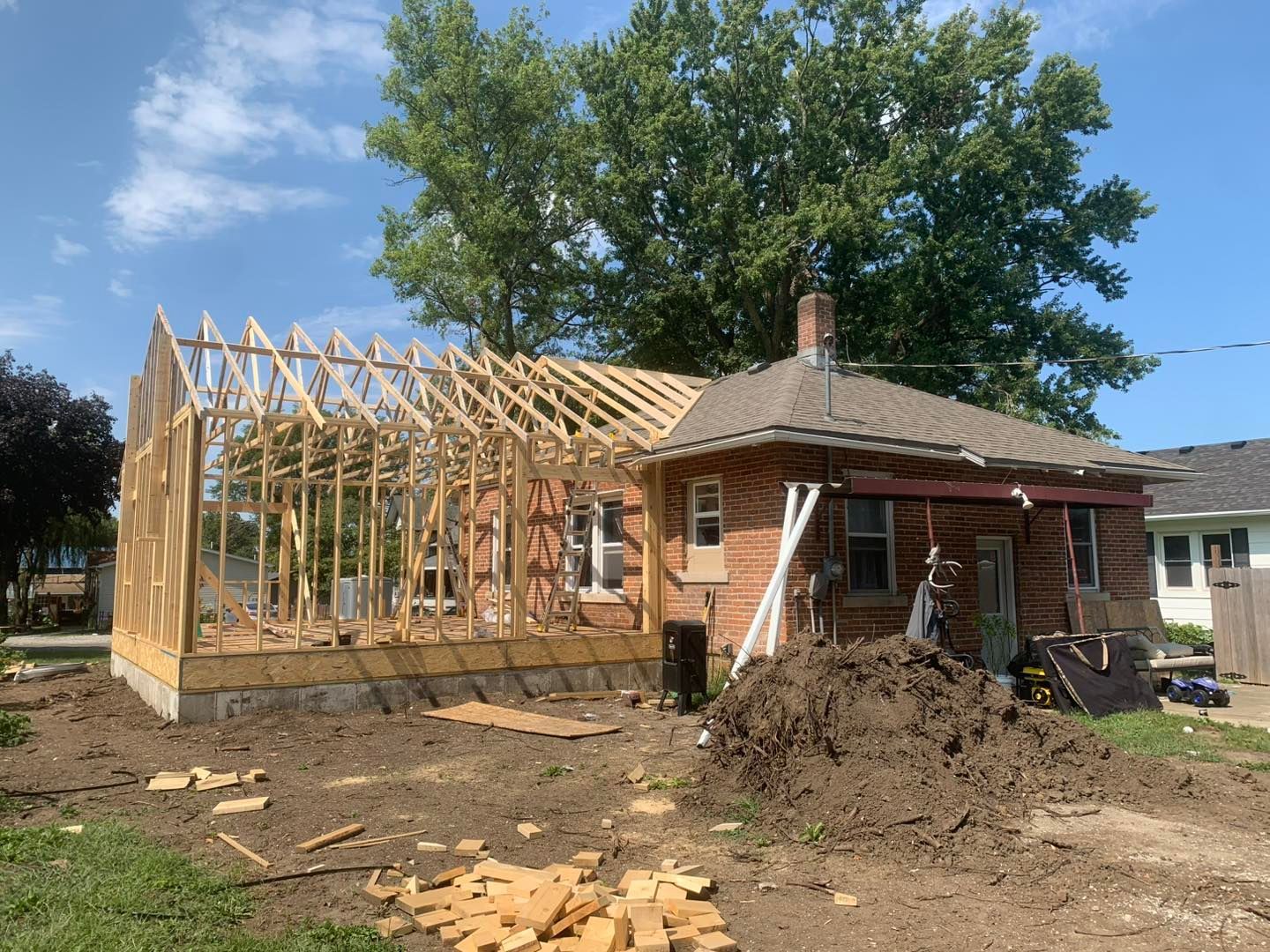 A brown brick house under renovation with a newly framed wooden structure attached to its side.