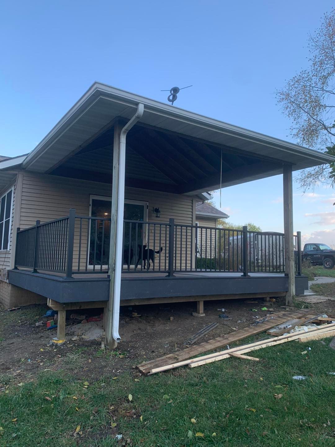 A raised deck with a dark railing and roof overhang attached to the back of a house.