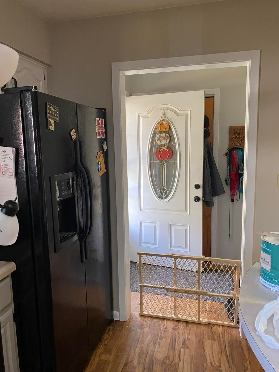 A black refrigerator stands next to a doorway featuring a white door with an oval glass insert and a wooden baby gate.