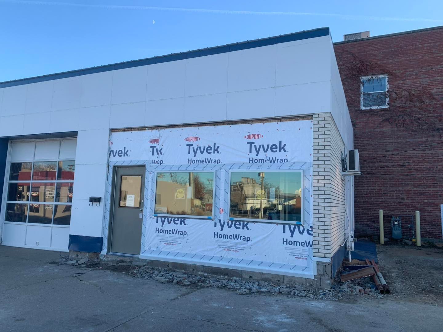 A commercial building under renovation with exposed white Tyvek wrap, new windows, and a partially finished brick corner.