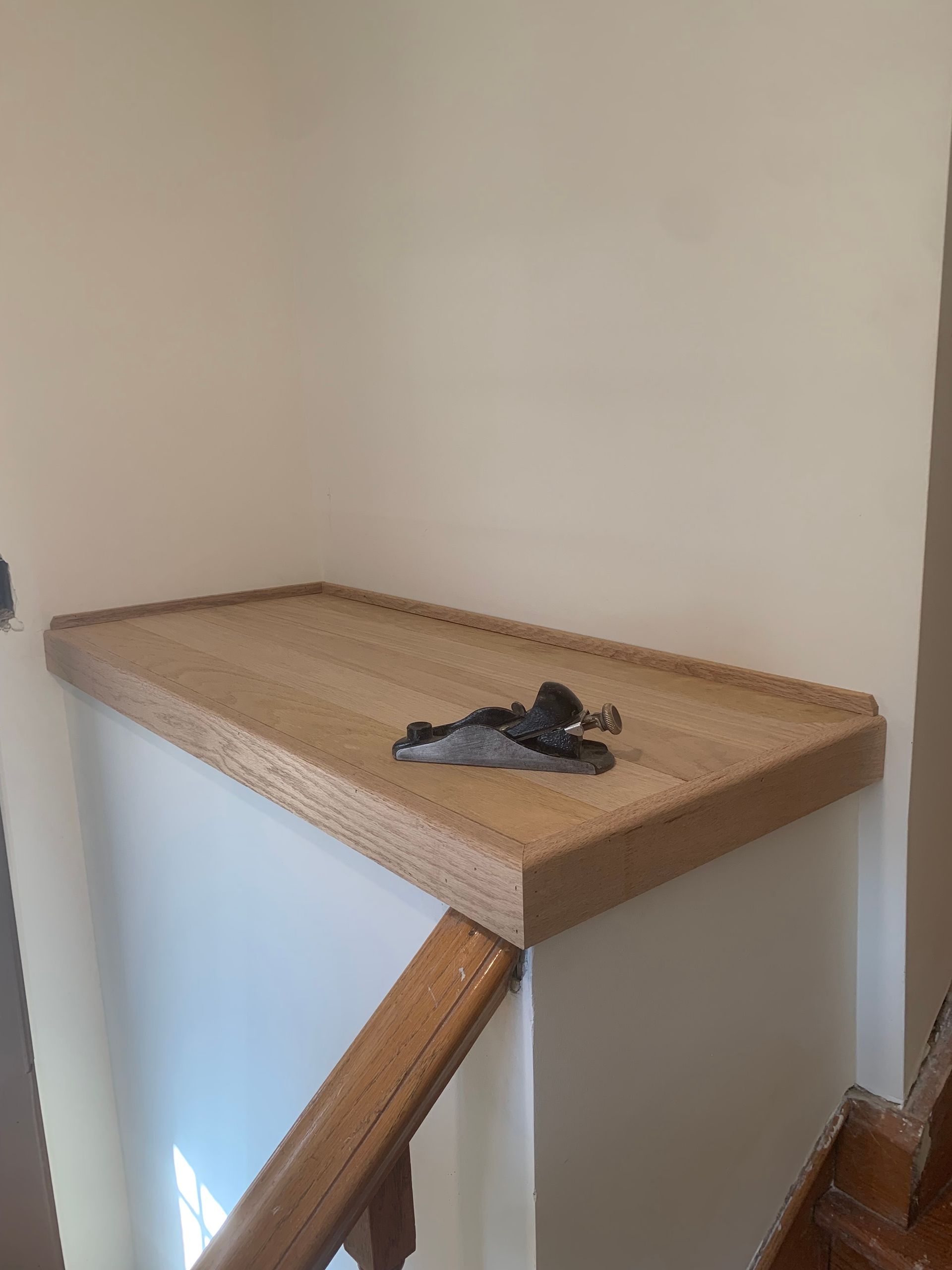 A small, dark wooden hand plane sits on a light-colored wooden ledge at the top of a staircase.