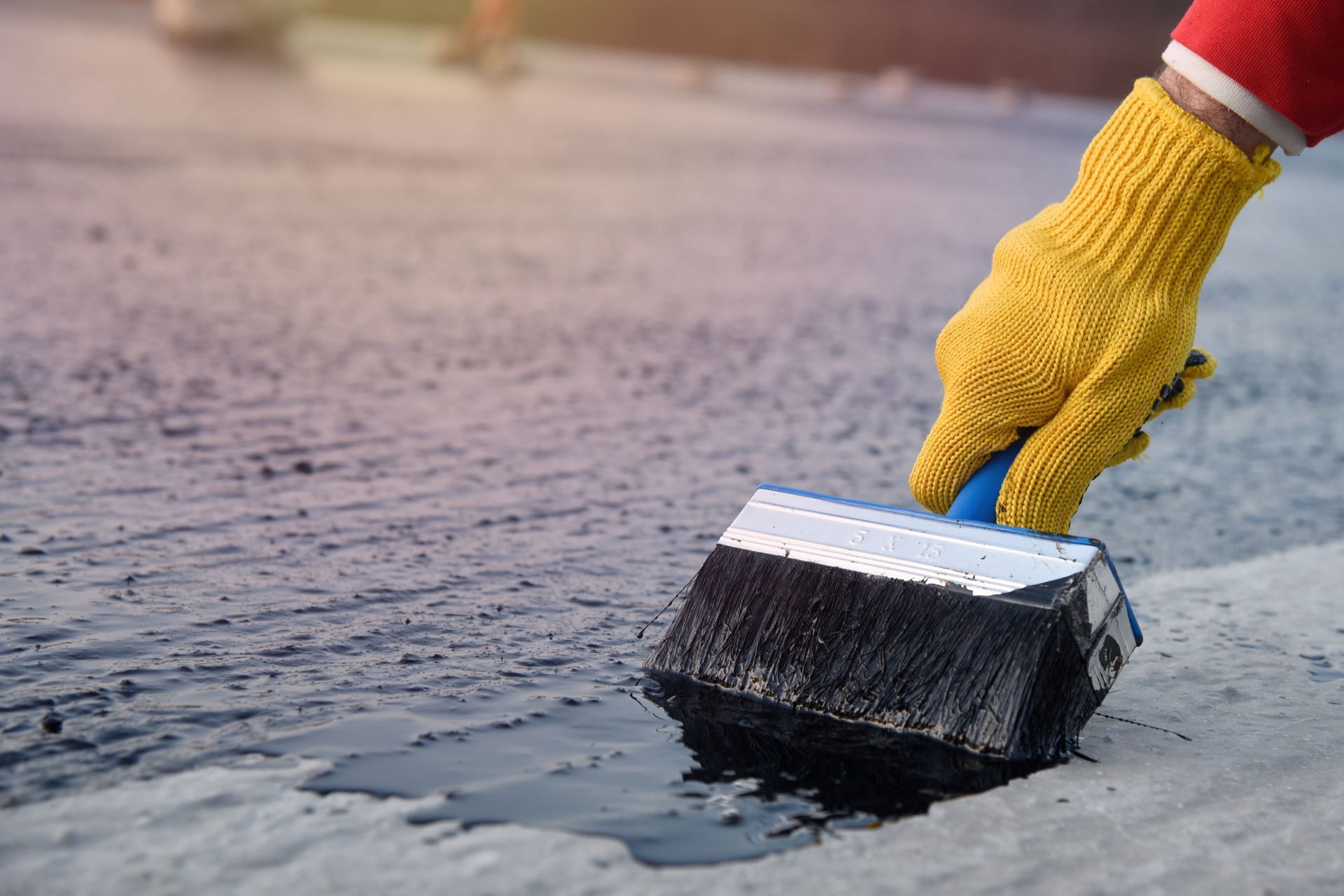 Close-up of a worker’s hand as it uses a thick paintbrush to apply bitumen mastic to a foundation.