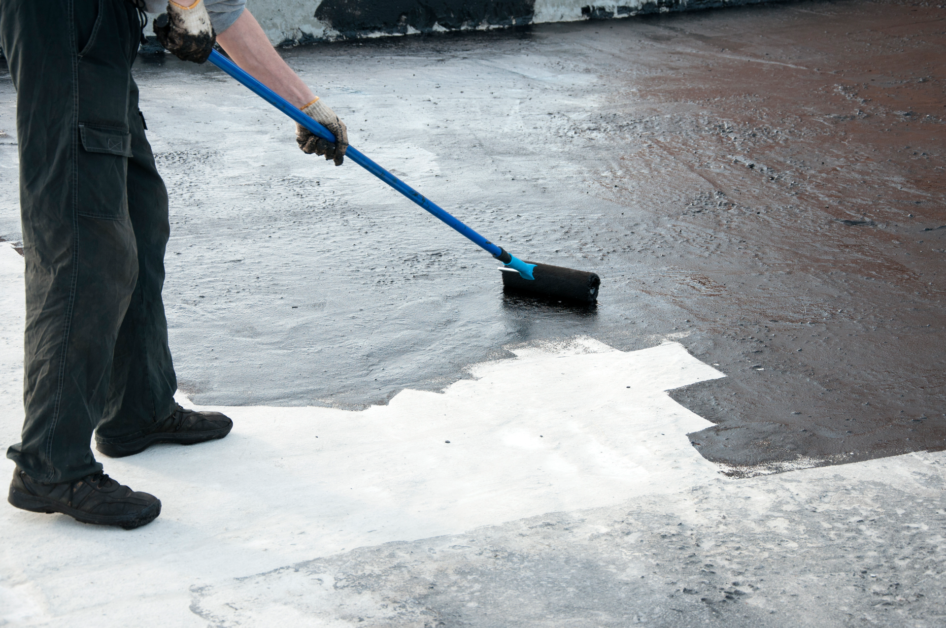 A man is putting bitumen primer on a roof for waterproofing.