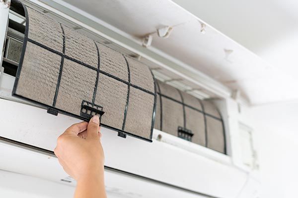 Close-up of dirty air filter being removed for cleaning, showcasing the need for air duct cleaning s