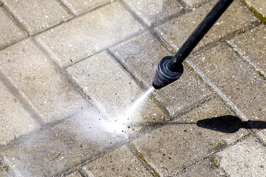 A person is using a high pressure washer to clean a brick walkway.