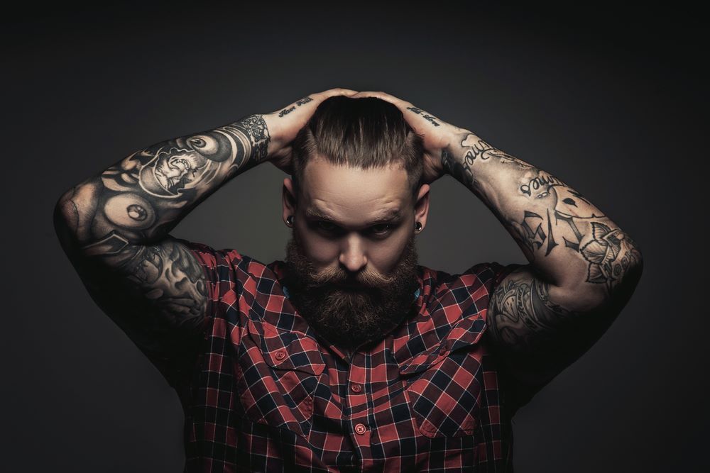 A Man With a Beard and Tattoos on His Arms is Holding His Head— Redback Ink Tattoo Studio in Kawana, QLD
