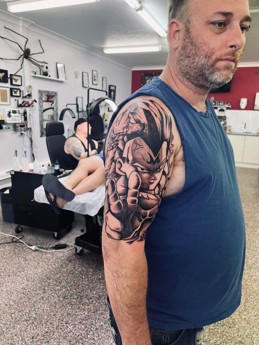 a man with a tattoo on his arm is standing in a tattoo shop - Tattoo Studio in Kawana, QLD