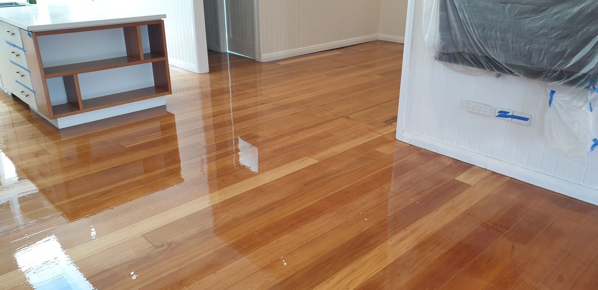 Shiny Wooden Floor Reflecting Light, With A Bookshelf And Protected Wall Visible — Timbertop Floor Sanding & Polishing In Port Douglas, QLD