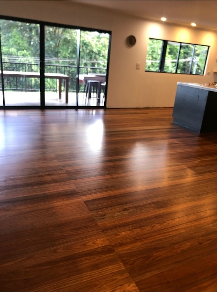Glossy, Dark-stained Wooden Floor In A Bright Room With Large Glass Doors And Windows Overlooking Greenery — Timbertop Floor Sanding & Polishing In Port Douglas, QLD
