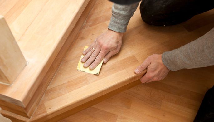 A Person is Sanding a Wooden Staircase With a Sandpaper — Timbertop Floor Sanding & Polishing In Tablelands, QLD