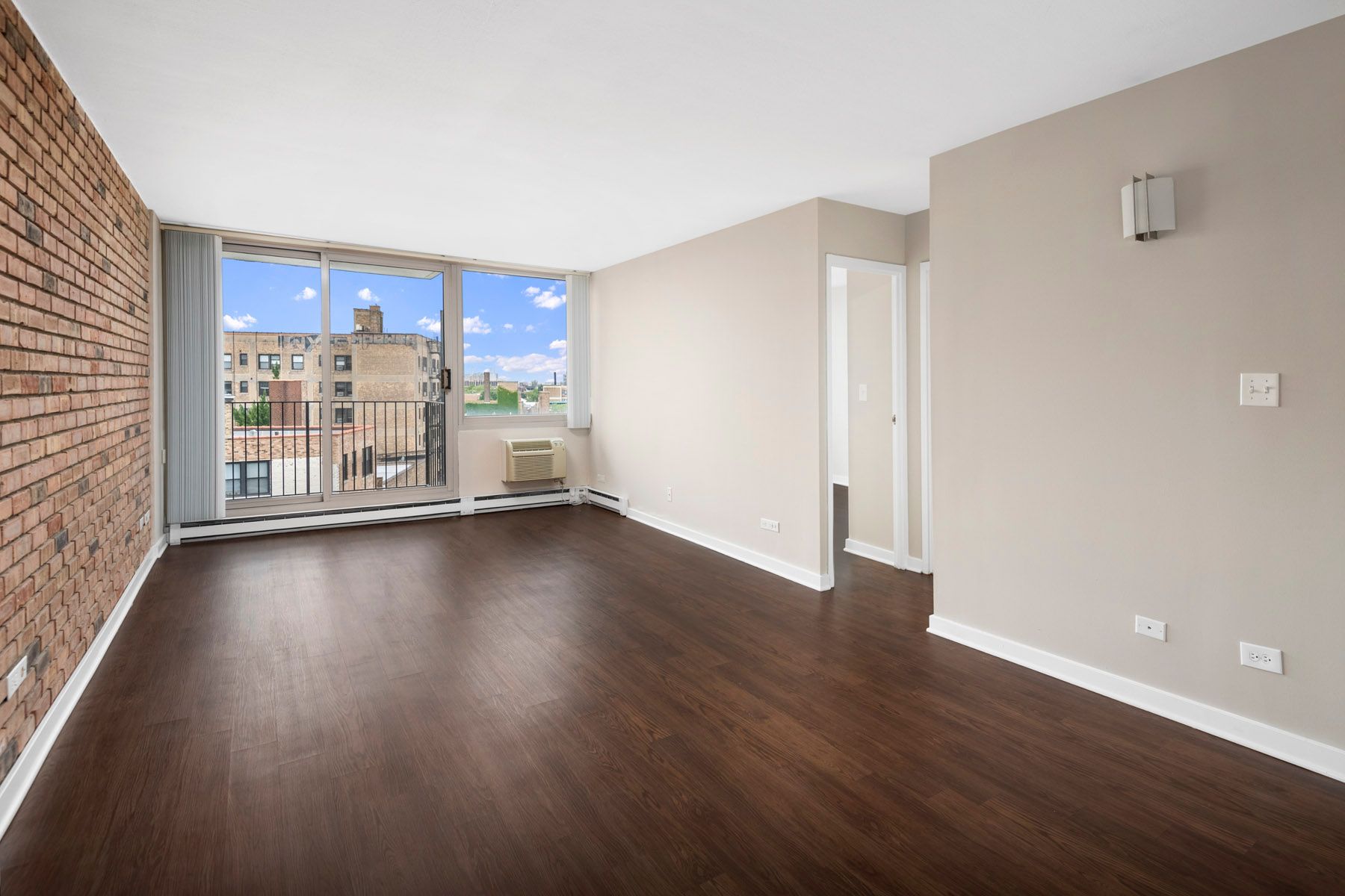 An empty living room with hardwood floors and a balcony at Park Lincoln by Reside.