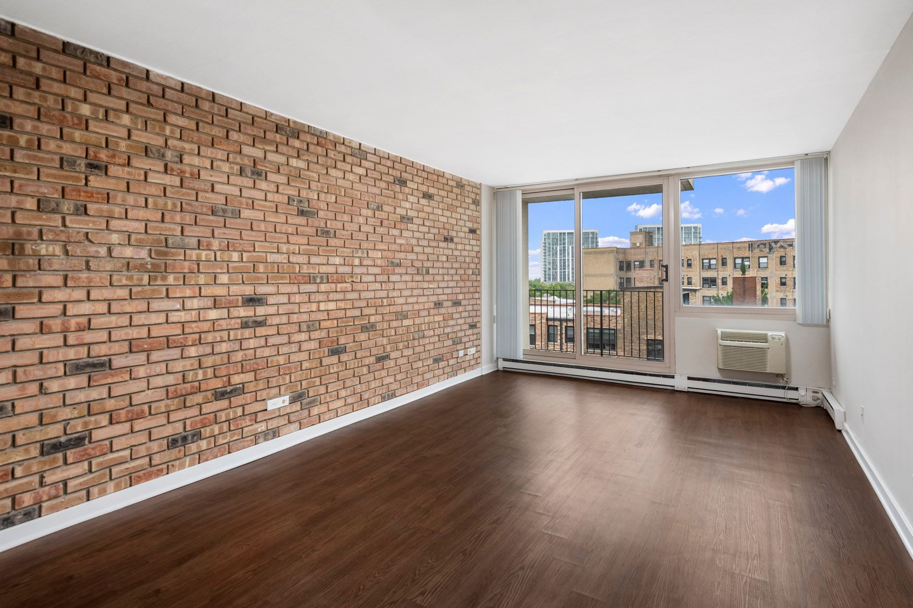 An empty living room with a brick wall and a balcony at Park Lincoln by Reside.