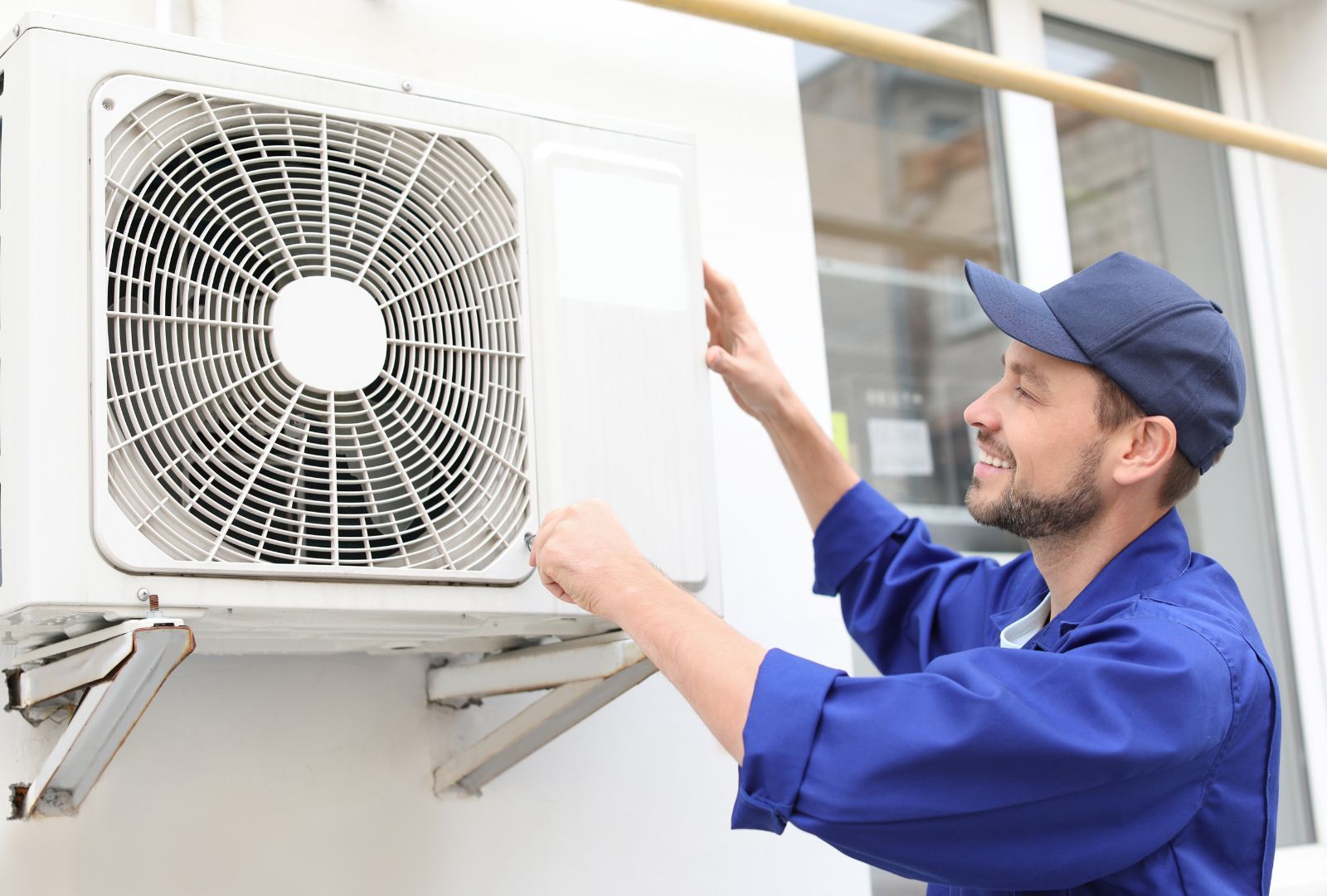 A man is fixing an air conditioner on the side of a building.