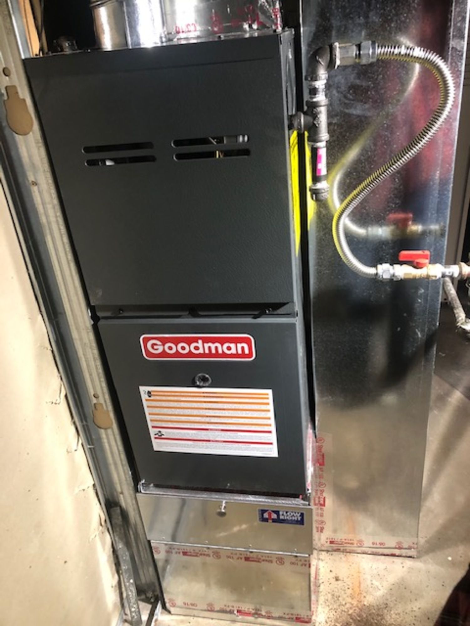 A goodman gas furnace is sitting in a garage next to a door.