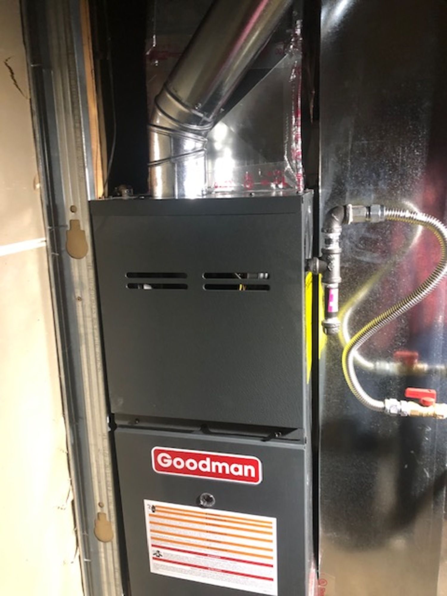 A goodman gas furnace is sitting in a room next to a door.