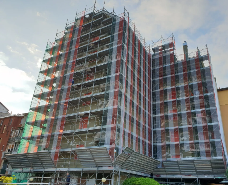 Edificio in costruzione, coperto da impalcature e reti di sicurezza, vista esterna.
