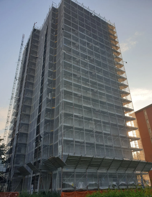 Un alto edificio in costruzione, coperto da impalcature e reti di sicurezza, vista esterna.