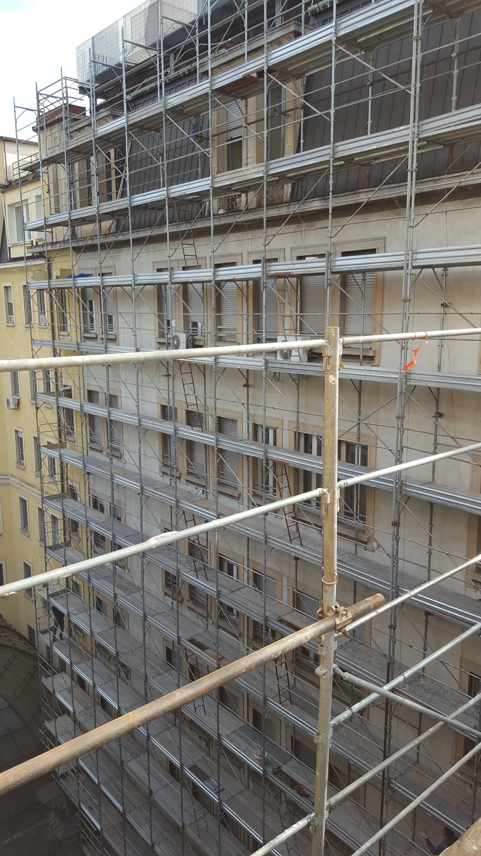 Esterno dell'edificio in fase di ristrutturazione con impalcature. Facciata beige, finestre e impalcature metalliche.