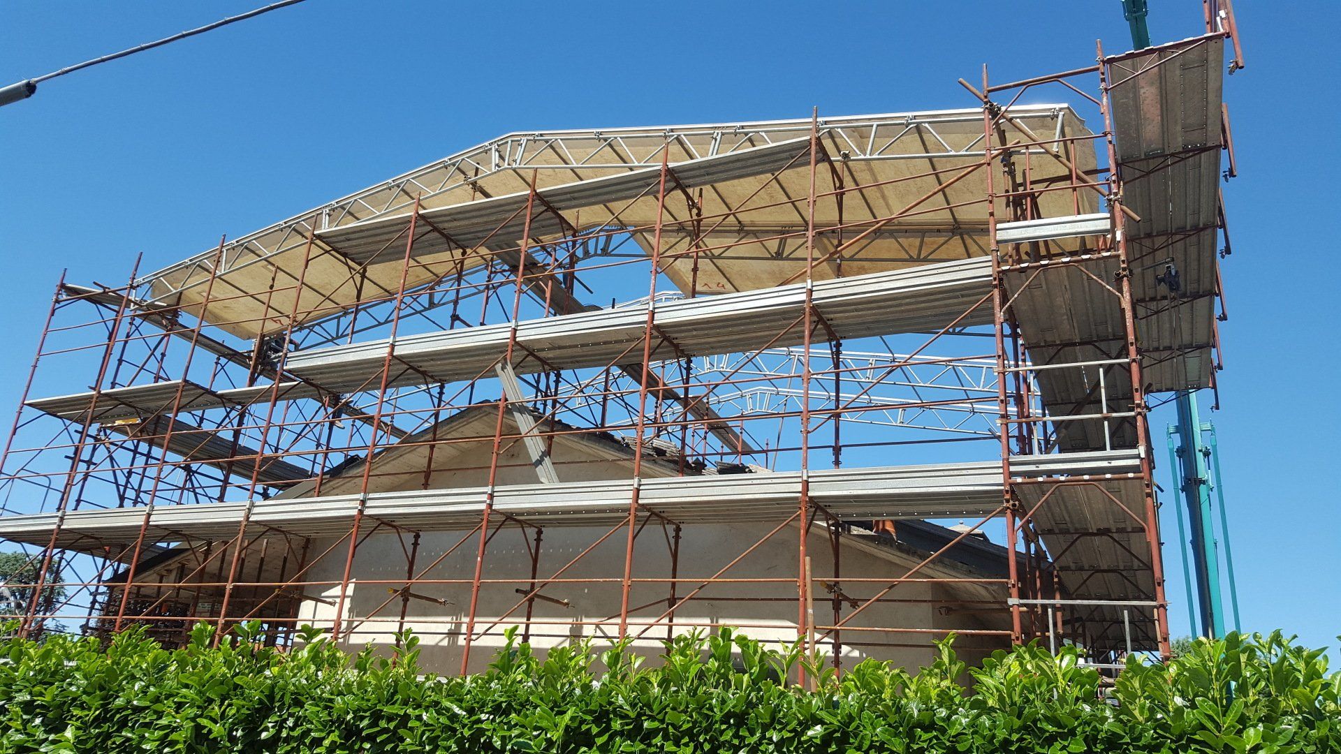 Edificio in fase di ristrutturazione, coperto da impalcature e teli protettivi, contro un cielo azzurro.