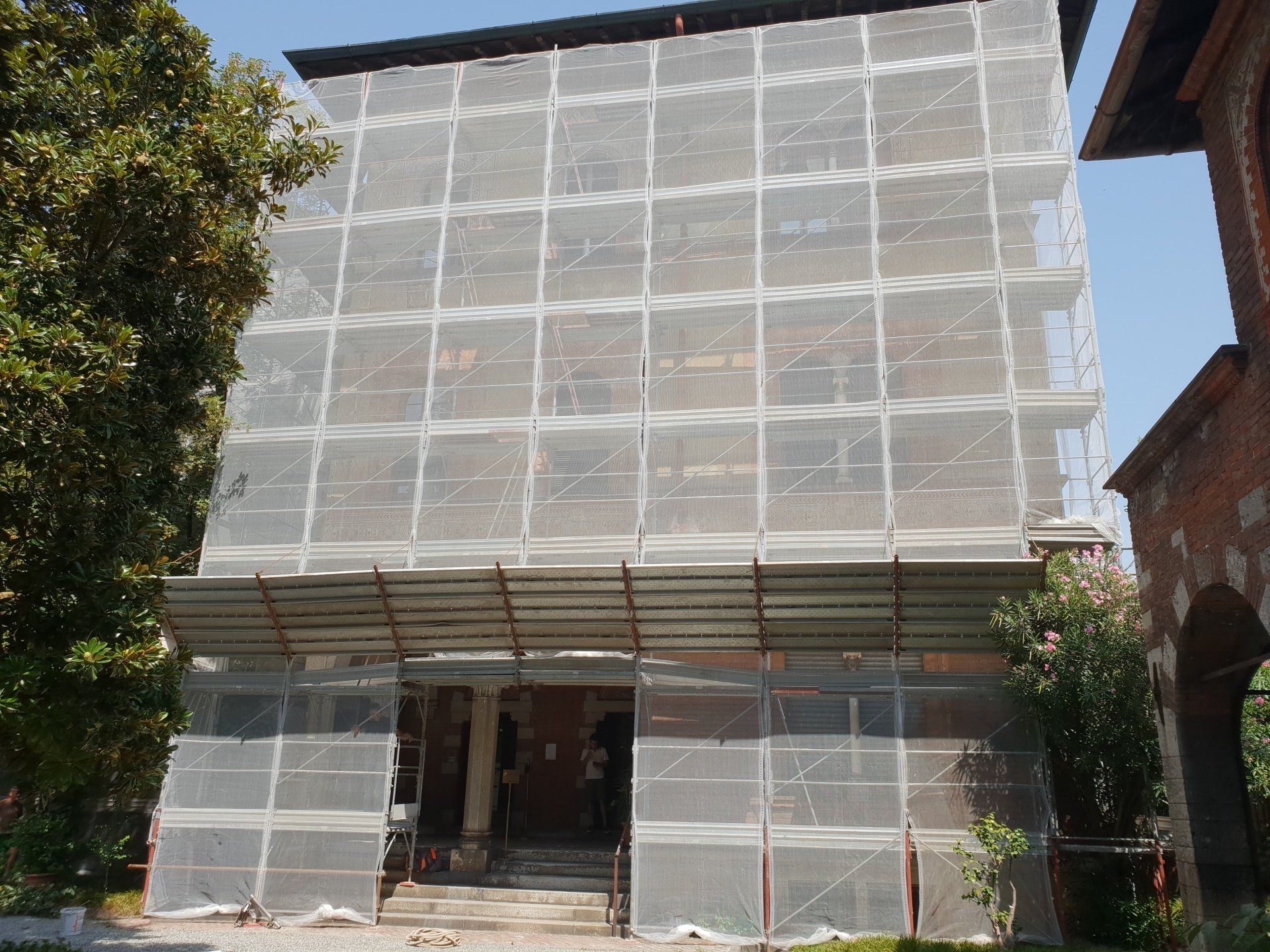 Edificio coperto da impalcature e reti, che suggeriscono lavori di ristrutturazione.