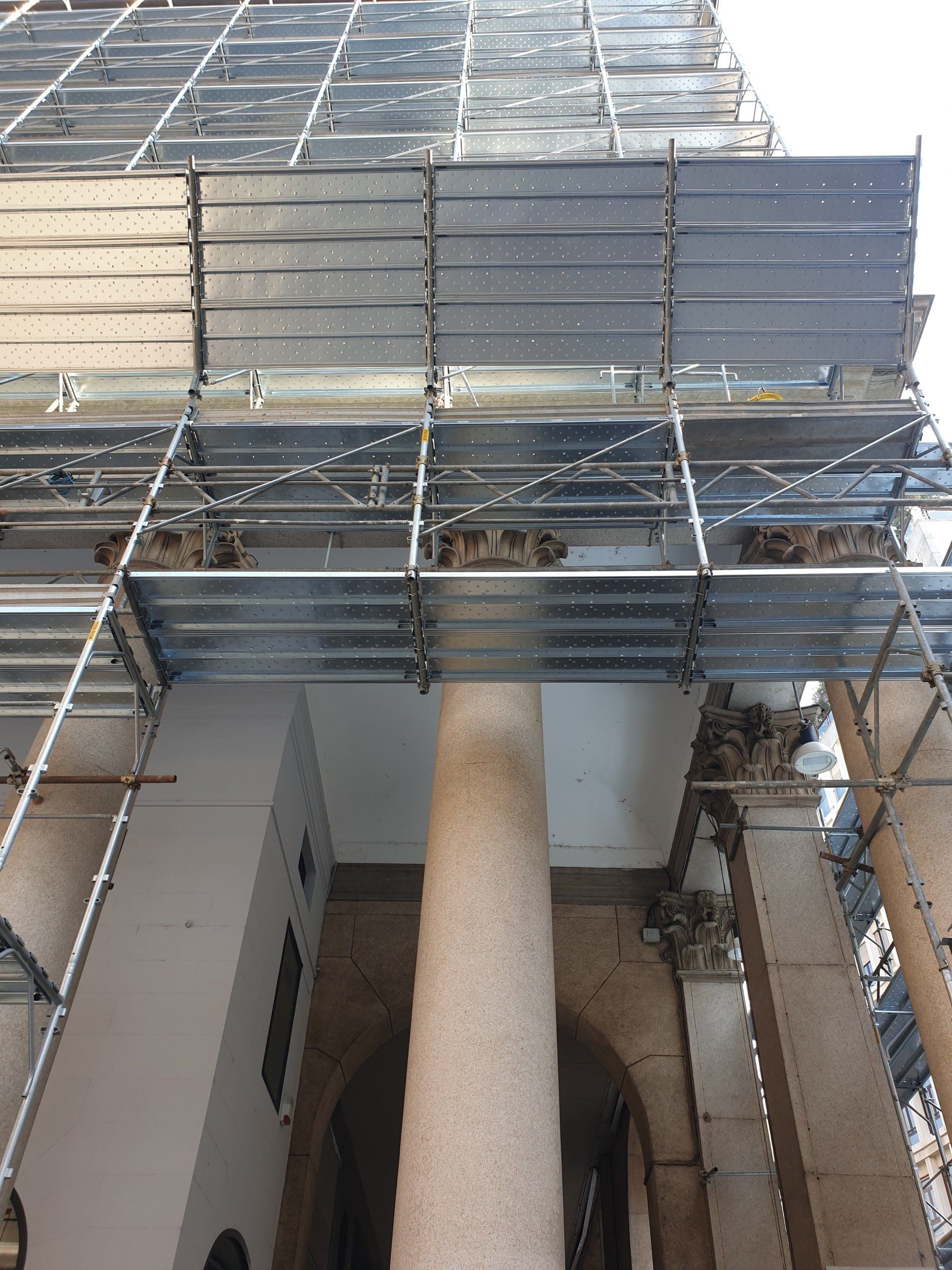 Un'impalcatura circonda l'alta colonna di un edificio. Piattaforme di metallo grigio si elevano verso l'alto.