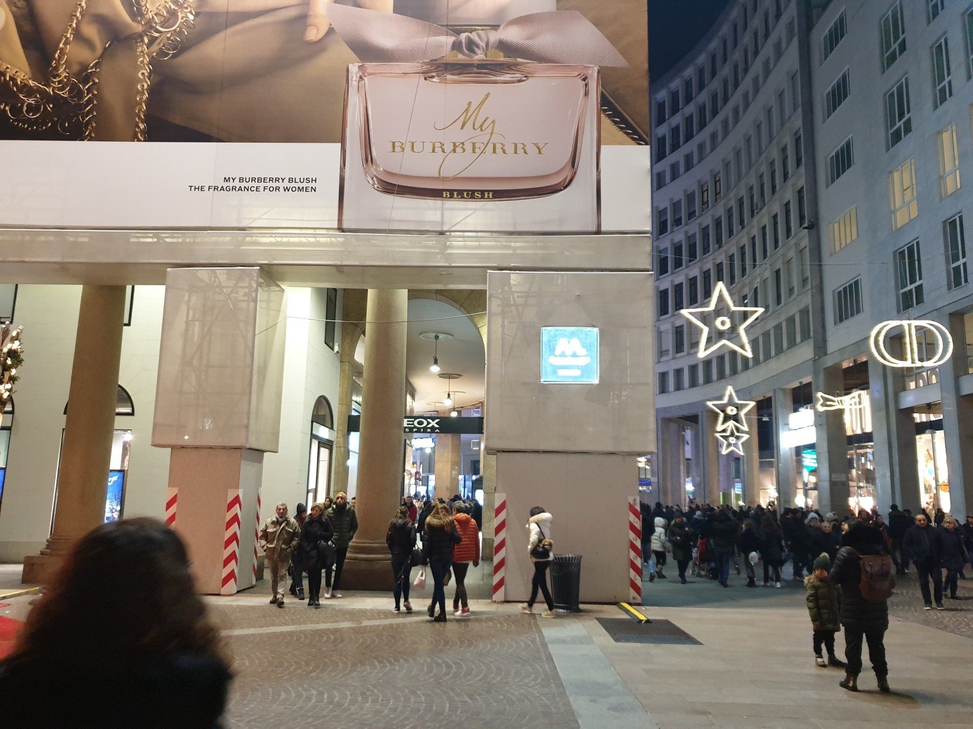 Persone in una strada cittadina di notte, con negozi e una grande pubblicità di Burberry.