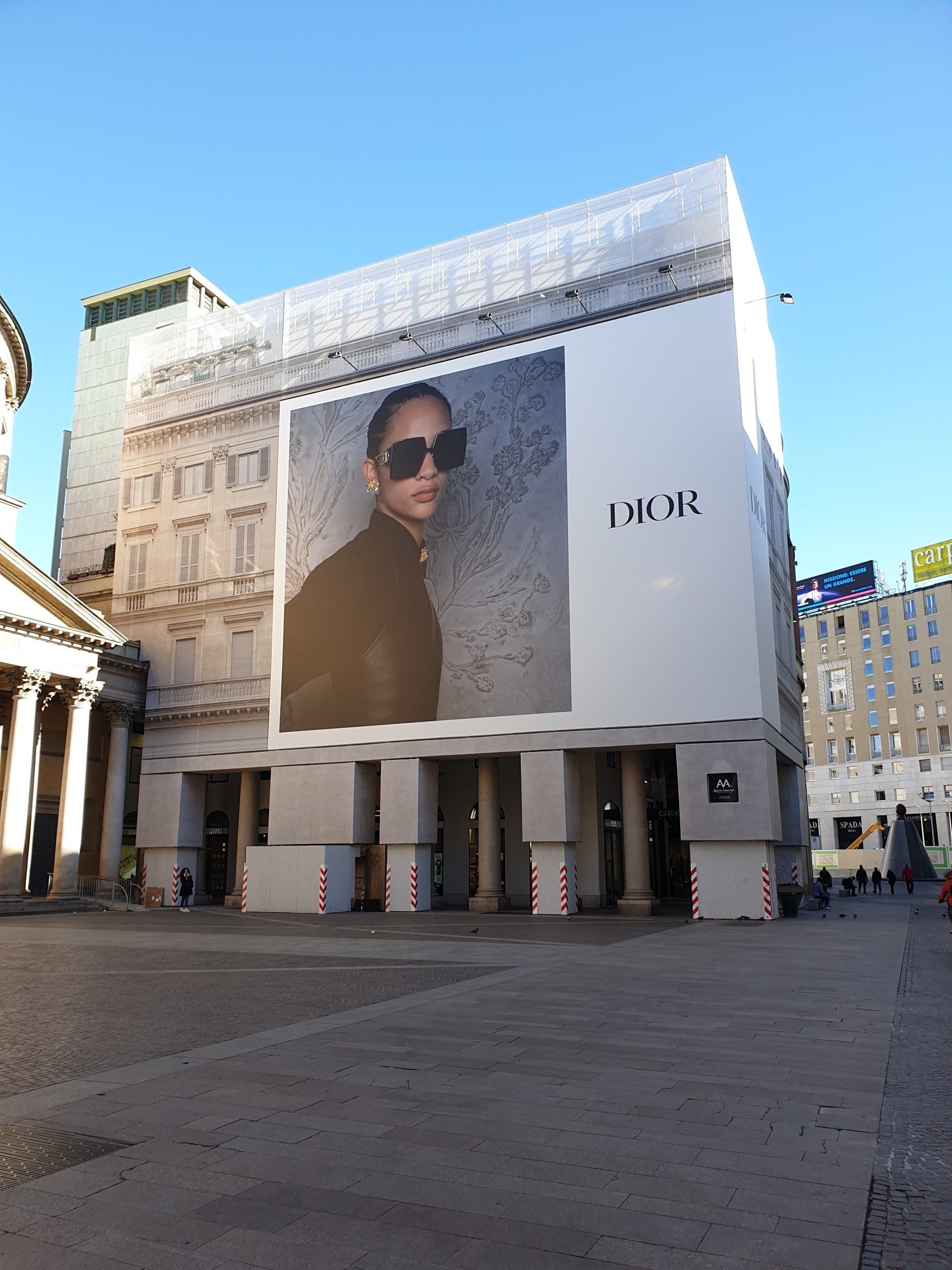 Grande pubblicità Dior sulla facciata di un edificio. La pubblicità mostra una persona con occhiali da sole, accanto al logo Dior.