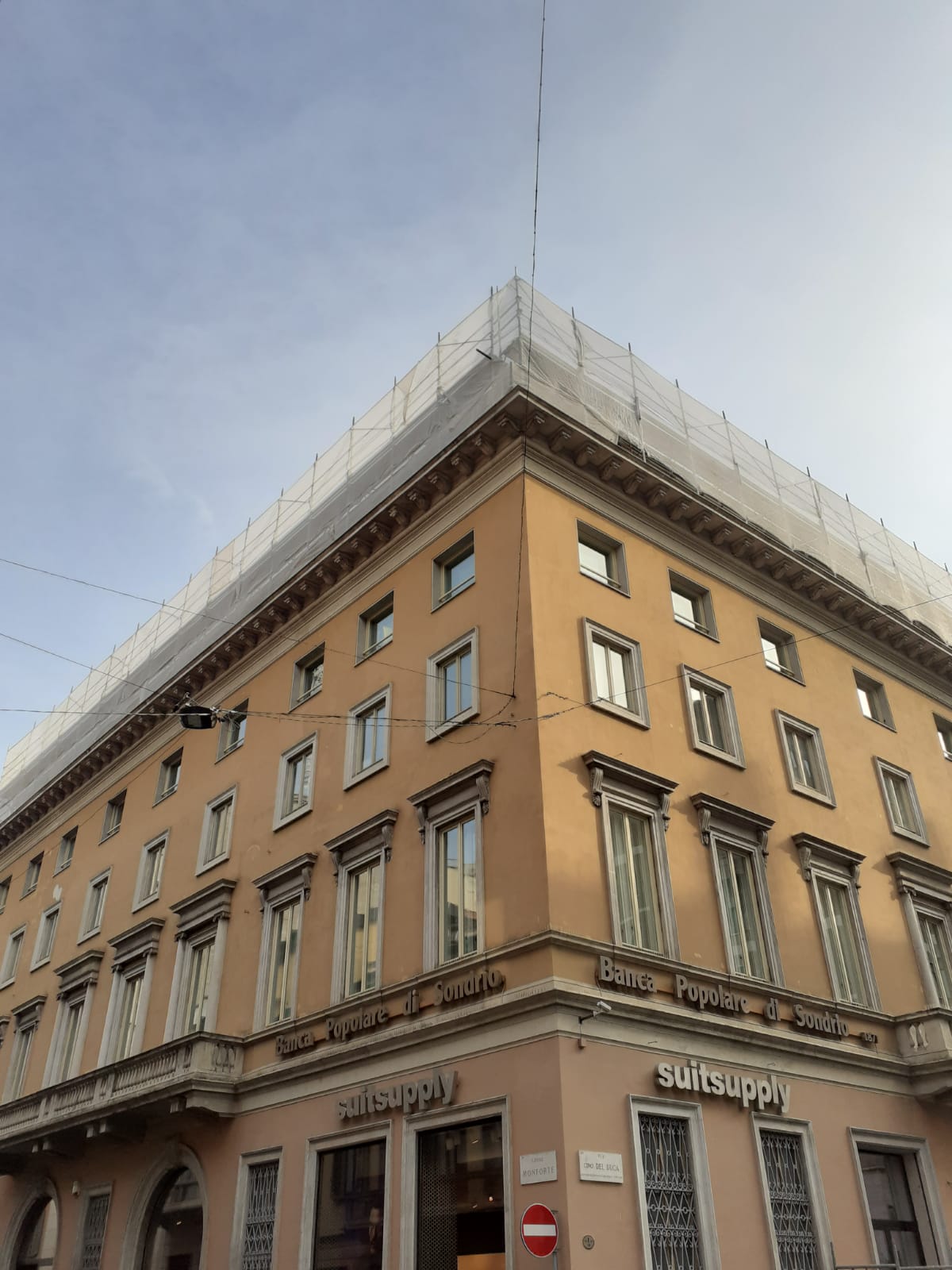 Angolo di un edificio con impalcature; facciata beige, numerose finestre; insegna del ristorante alla base.