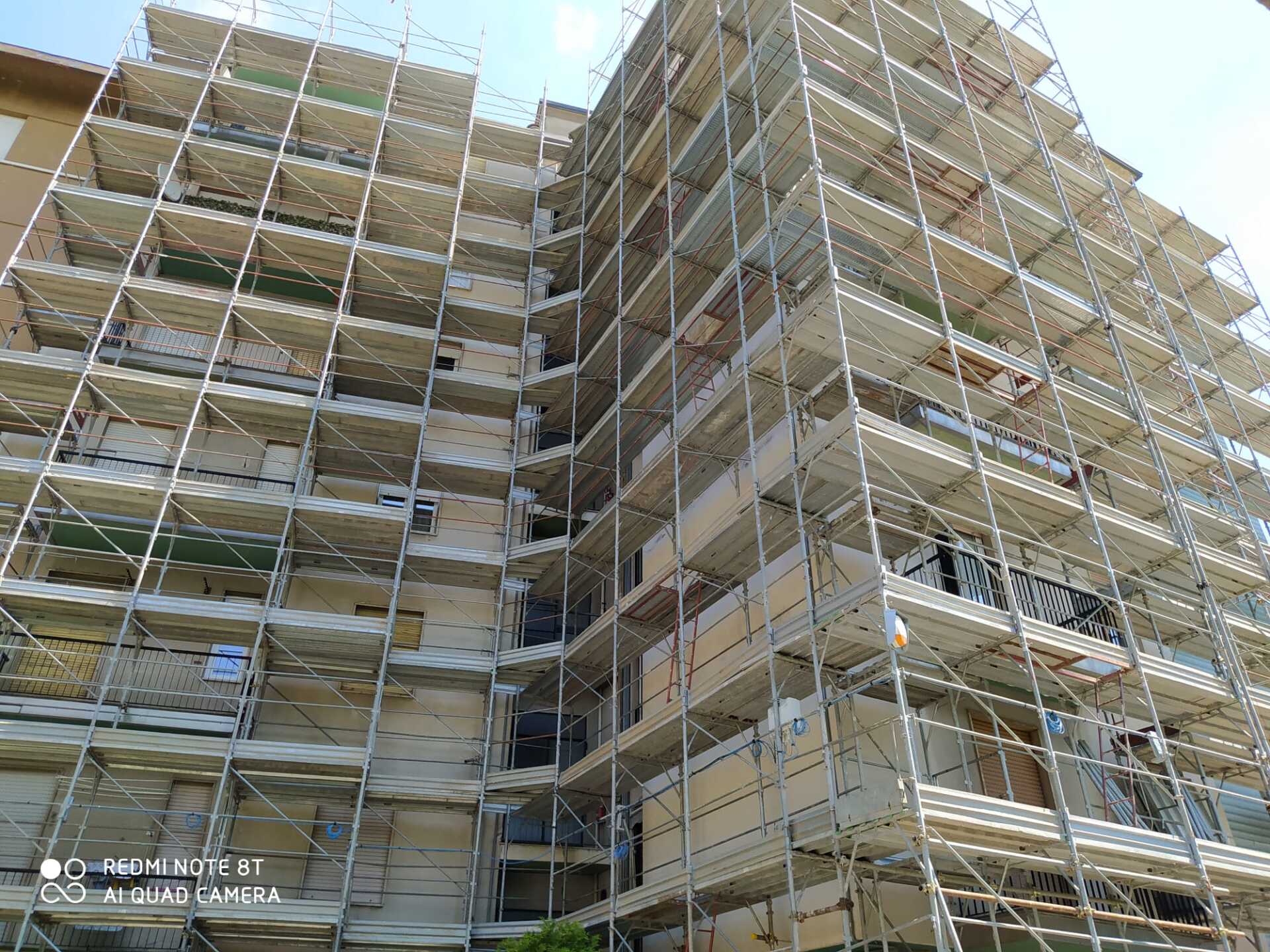 Edificio in costruzione, coperto da impalcature, contro un cielo luminoso.