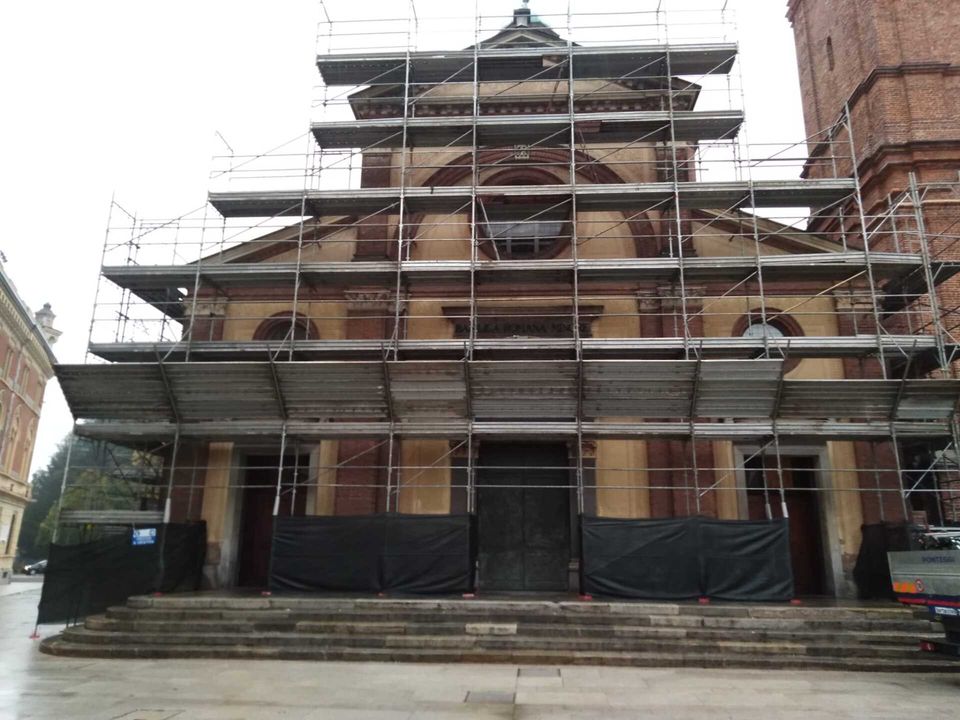 Facciata della chiesa in fase di ristrutturazione con impalcature. Edificio beige e marrone con gradini.