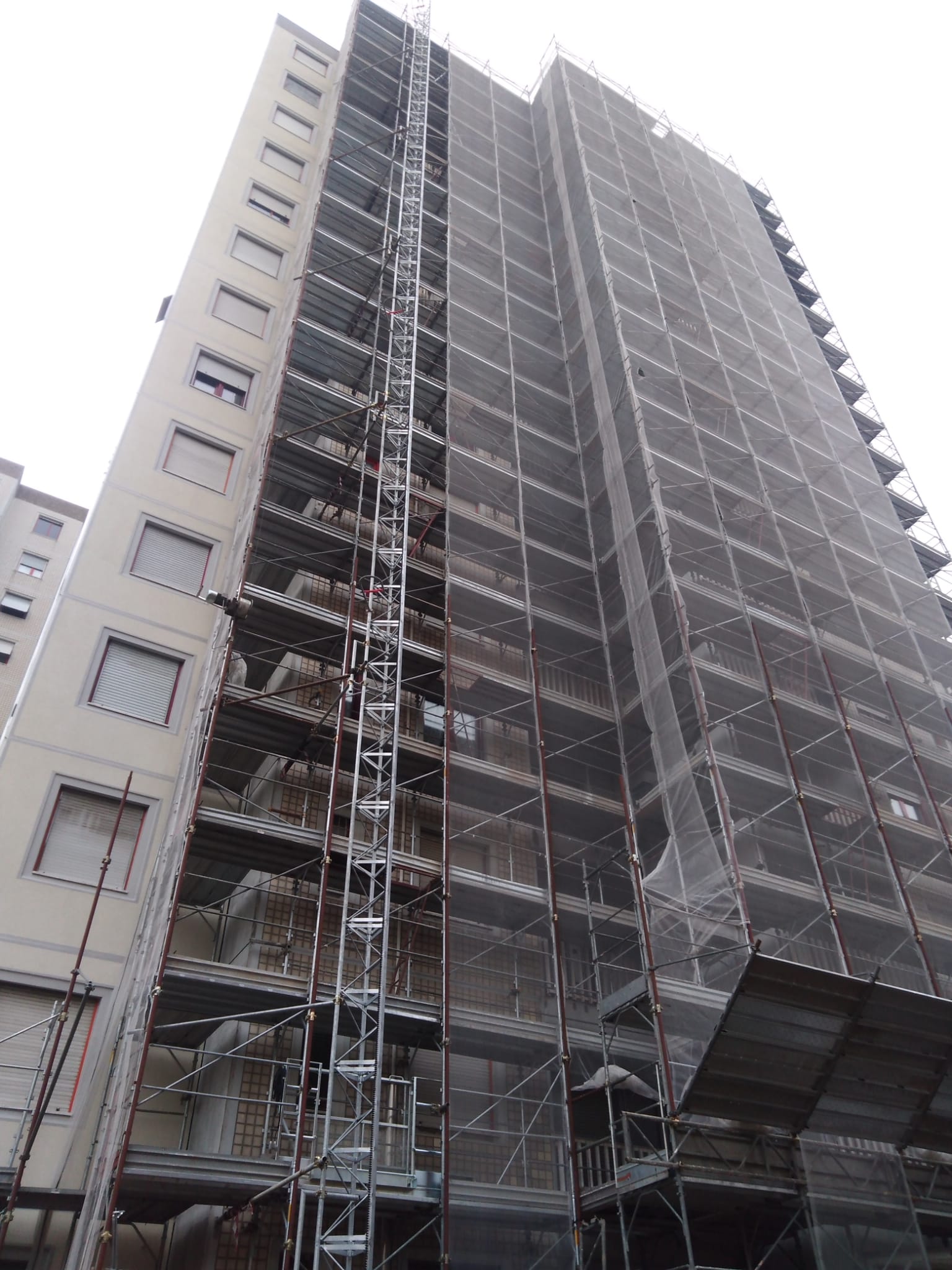 Edificio alto coperto da impalcature e reti di sicurezza, in costruzione.