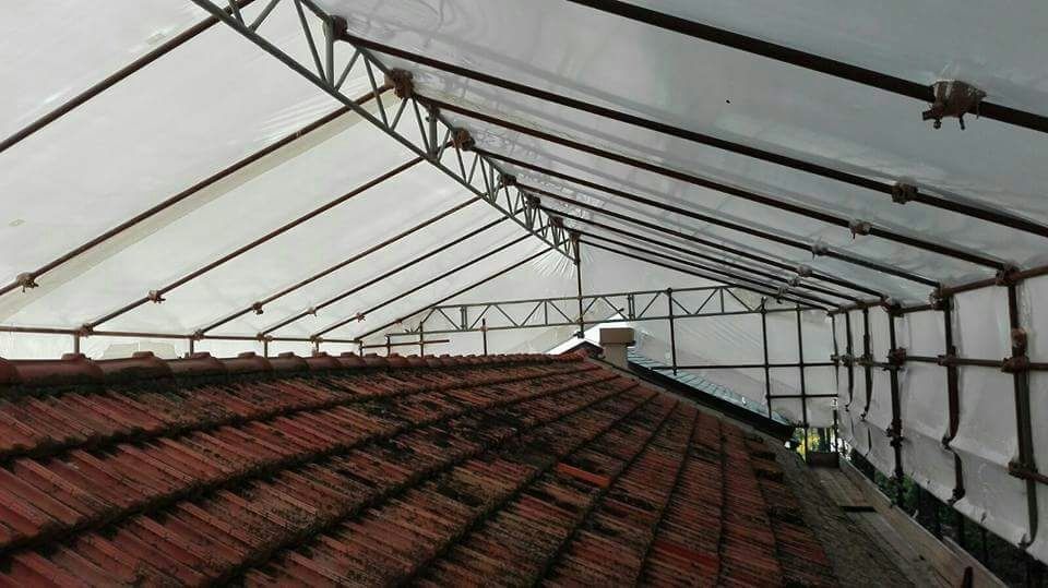 Tetto in tegole sovrapposte coperto da un telo bianco sostenuto da una struttura metallica.