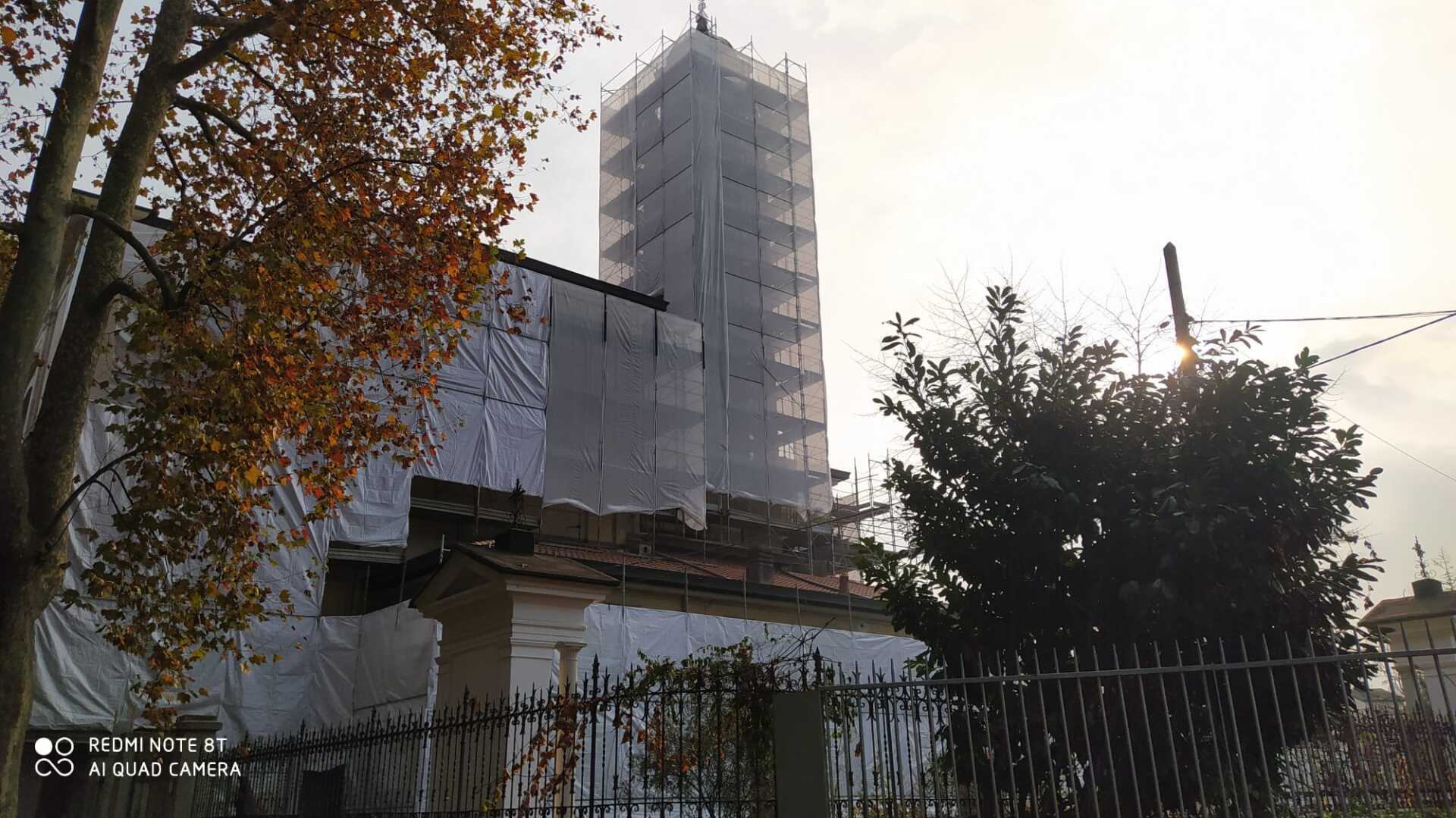 Edificio in fase di ristrutturazione, avvolto da un involucro protettivo. Un'alta torre si erge, parzialmente nascosta.
