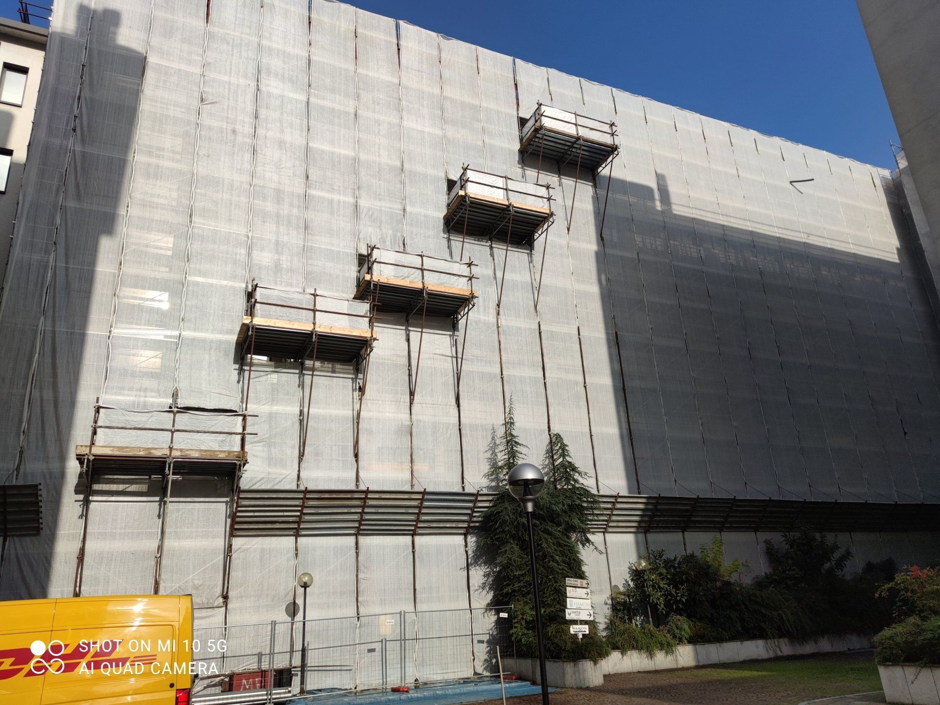 Edificio in costruzione con impalcature e piattaforme, ricoperte da una rete grigia.