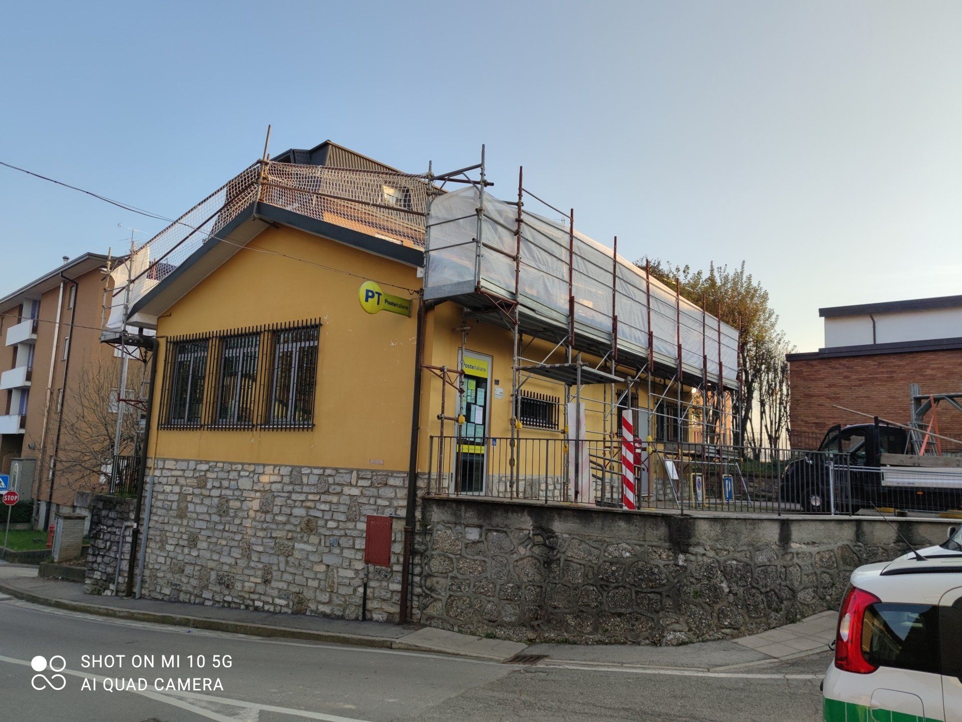 Edificio giallo in fase di ristrutturazione con impalcature; base in pietra, cielo azzurro e auto parcheggiata sulla strada.