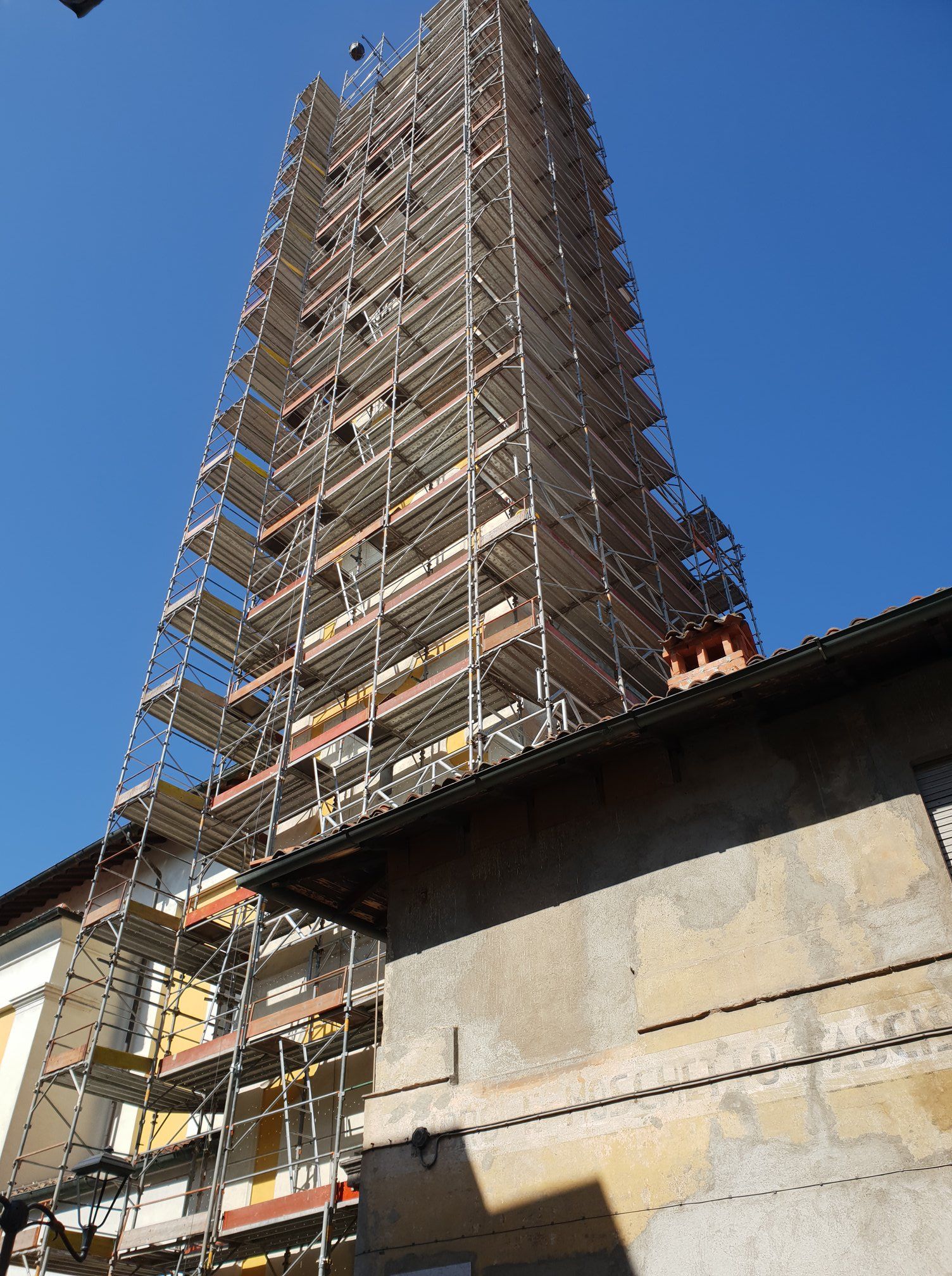 Edificio alto in fase di ristrutturazione, racchiuso tra impalcature e contro un cielo azzurro.