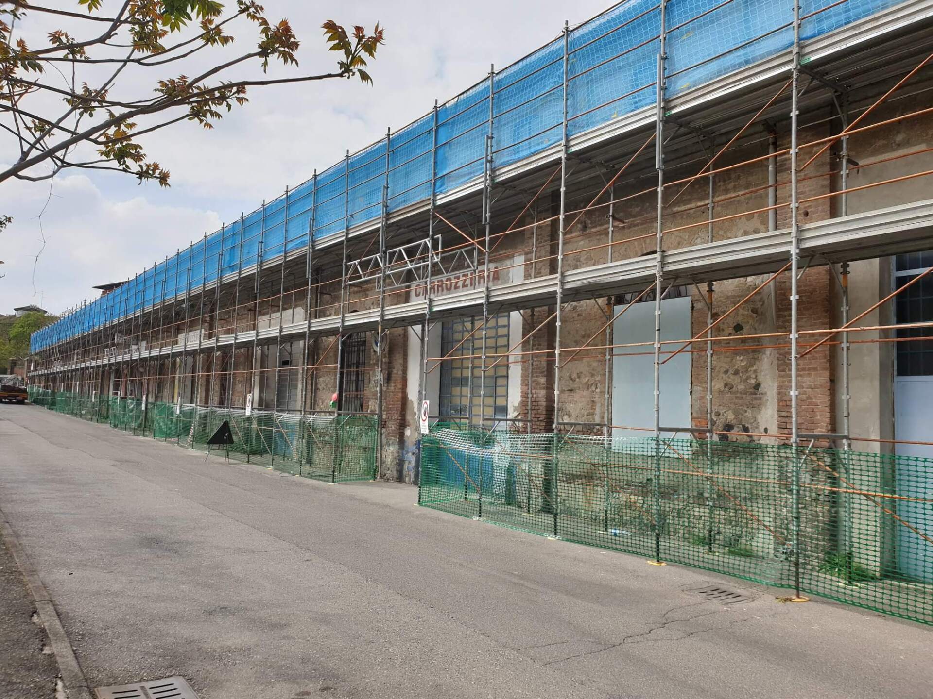 Edificio in fase di ristrutturazione con impalcature e reti di sicurezza lungo una strada.