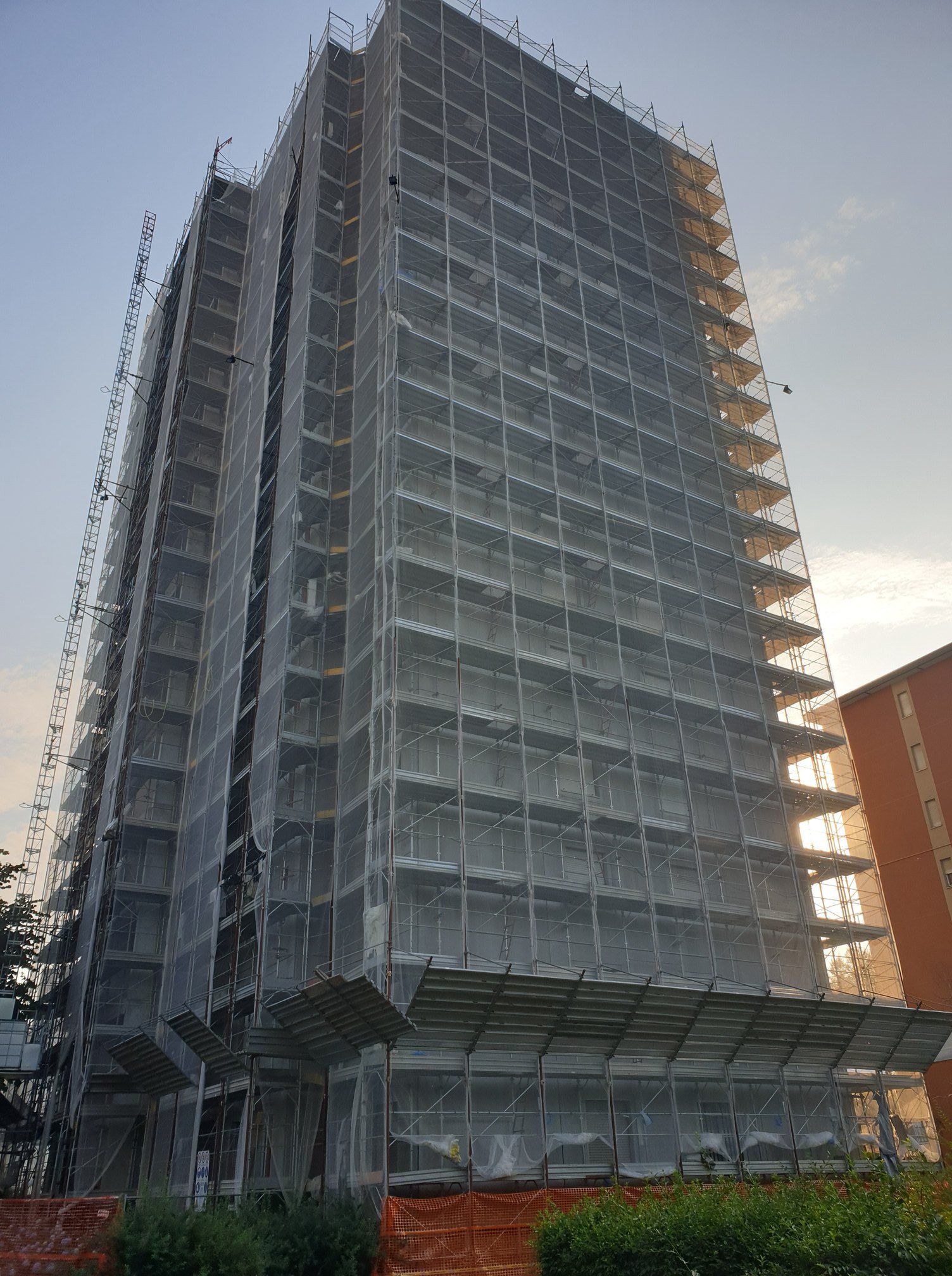 Edificio alto in costruzione, coperto da impalcature e reti di sicurezza, base in mattoni.