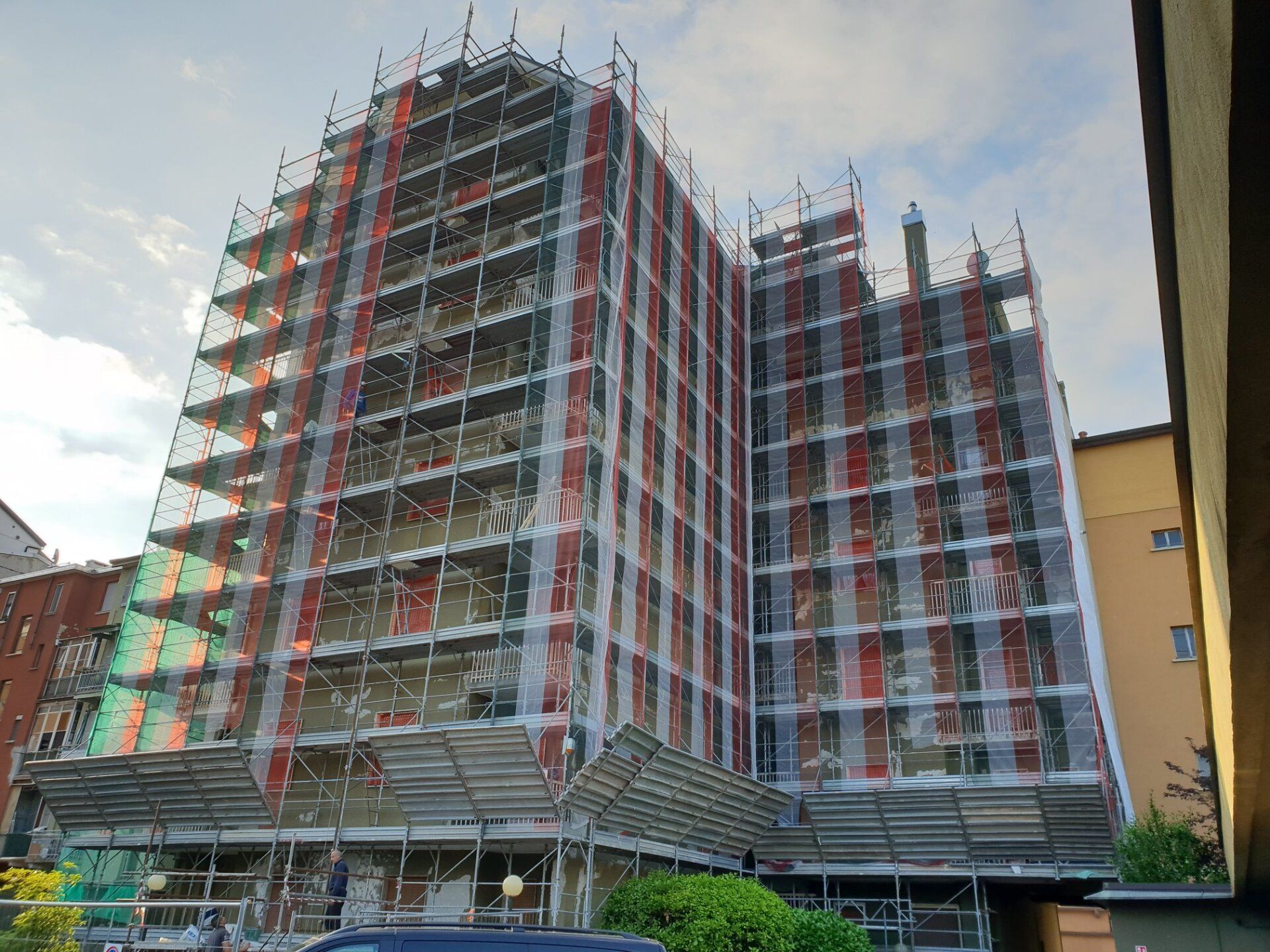 Edificio in costruzione, coperto da impalcature e reti di sicurezza, contro un cielo nuvoloso.