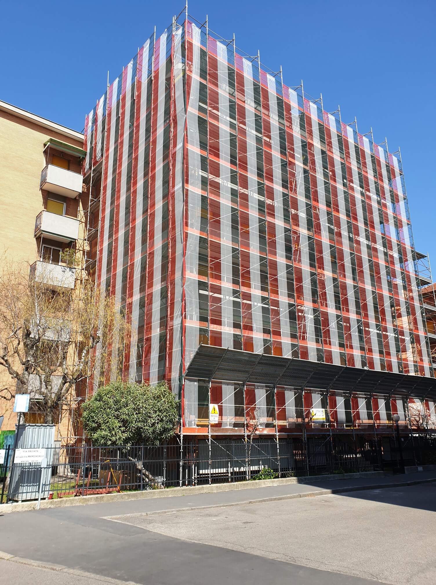 Facciata dell'edificio ricoperta da impalcature e reti di sicurezza, in fase di ristrutturazione.